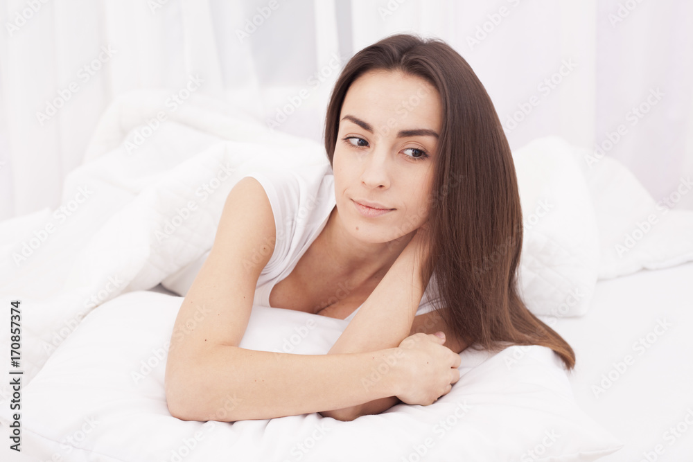 Young beautiful brunette woman lying on pillow in white bed and waking up. Young beautiful brunette woman lying on pillow in white bed and waking up.