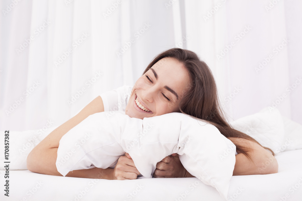 Young beautiful brunette woman lying on pillow in white bed and waking up.