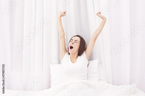 Brunette Woman stretching in white bed after wake up