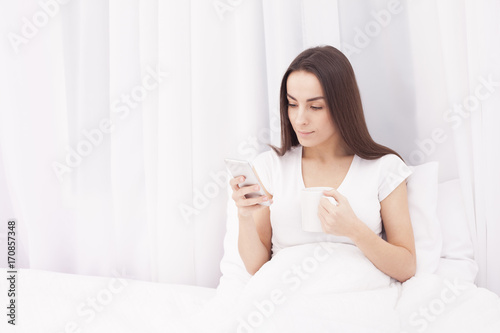 Free Download Young beautiful brunette woman with cup of morning coffee in white bed. - GFXLoad