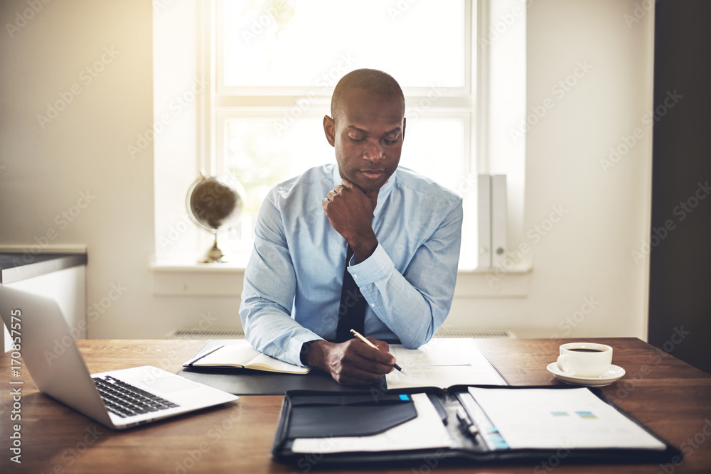 Focused young executive reading through paperwork at his desk Focused young executive reading through paperwork at his desk