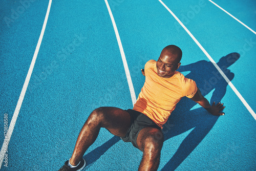 Smiling young runner resting on a running track after training