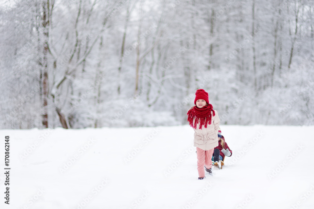 Two funny little girls having fun with a sleight in beautiful winter park. Cute children playing in a snow.