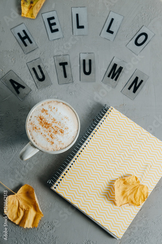 Flat lay comosition: letters with the text hello autumn, notebook and coffee on a gray background photo