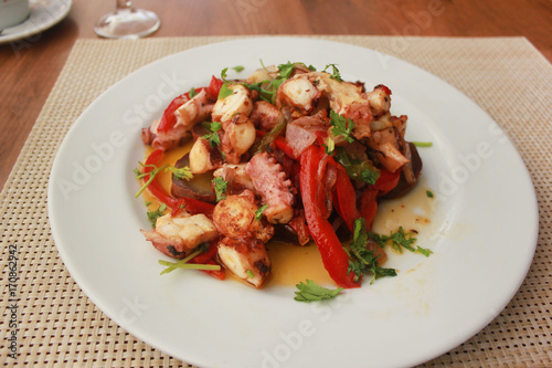 Seafood meal with fresh grilled octopus, sweet potatoes,onions, red bell pepper and parsley at restaurant set up table background. Delicious tasty small appetizer served on white plate for dinner. 