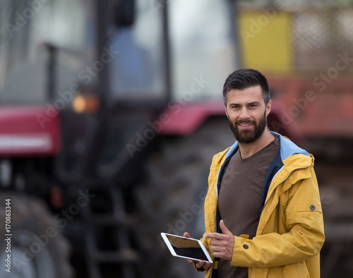 Farmer holding tablet with tractor behind