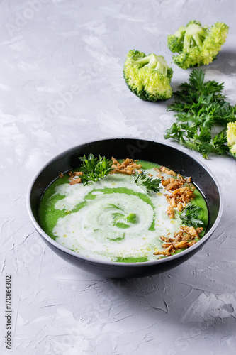 Vegetarian broccoli cream soup served in black bowl with cream, fried onion, fresh parsley and broccoli over over gray concrete background. Top view with space. Healthy eating.