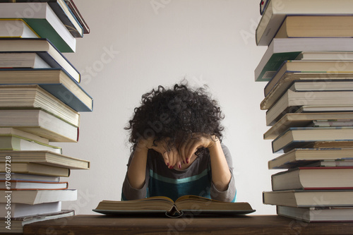 Erschöpfte Frau vor Buchstapel