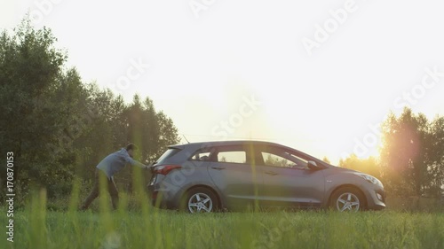 Young Man Pushing his Car Seen From the Side. Sunset