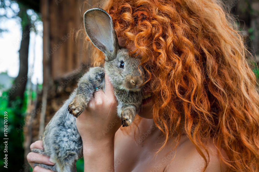 Obraz premium Beautiful girl with red hair on nature with a rabbit in her hands