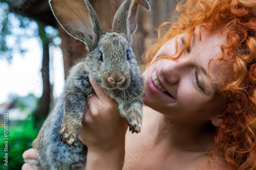 Beautiful girl with red hair on nature with a rabbit in her hands