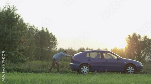 Young Man Pushing the Car Seen From the Side. Sunset