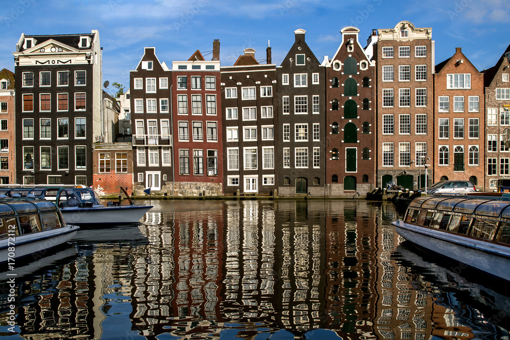 Traditional dutch medieval buildings in along the canal side,  reflected in water. Sunny day. Amsterdam, Netherlands.