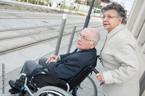 senior woman pushing husband in wheelchair to cross street