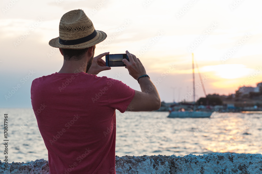 Obraz premium Young man tourist taking photo with smartphone by the sea