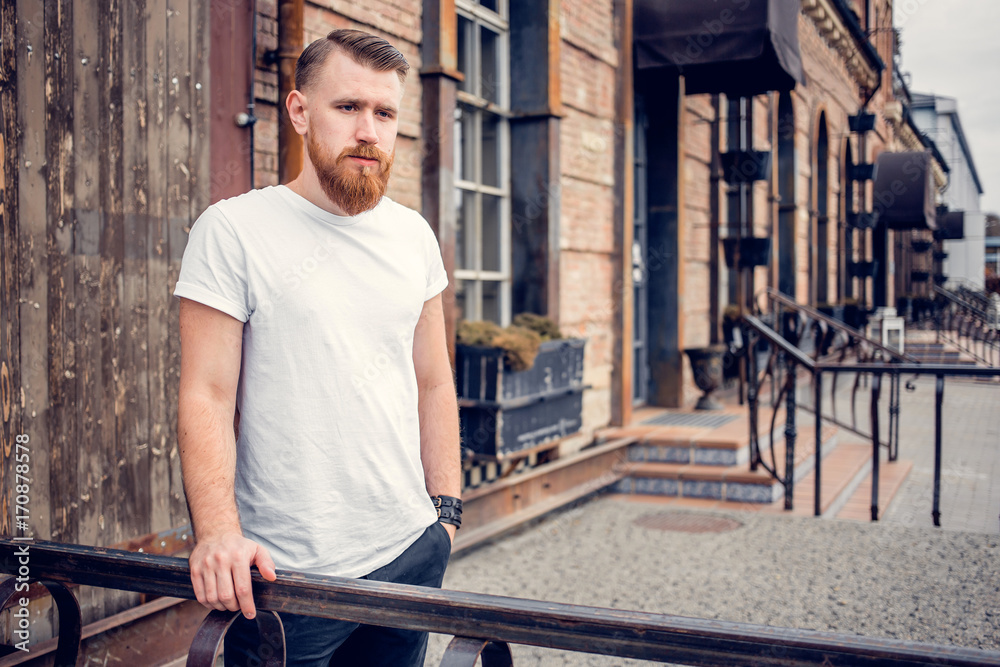 young guy with a beard and mustache posing on the street in the sunlight, fashion man, style, vintage style, retro men, handsome beard, outdoor portrait, hipster man