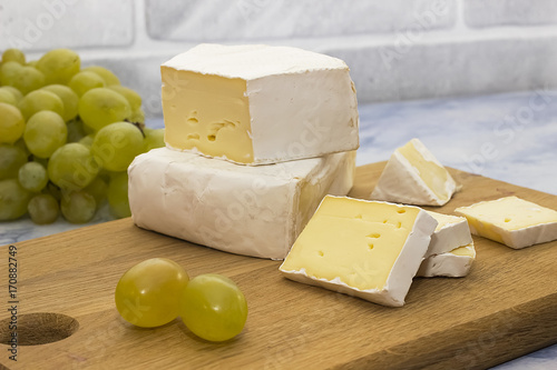 Camembert or brie cheese on a wooden board and green grapes