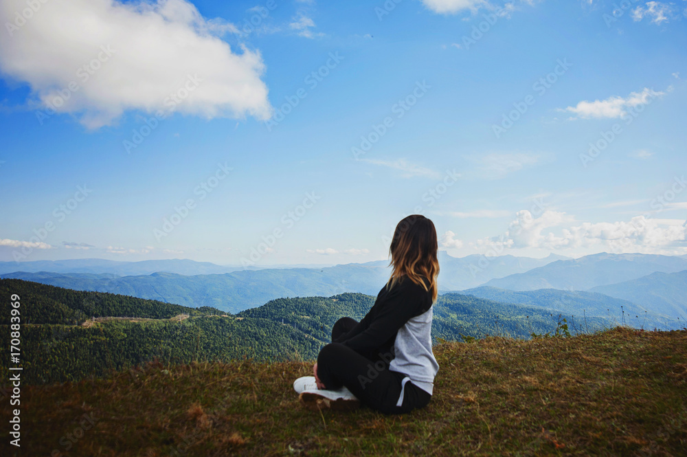 Young woman sitting on cliff's edge and looking to a sky with clouds
