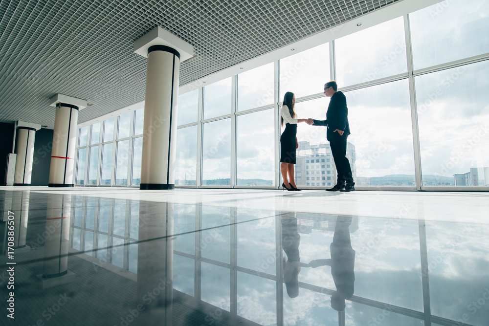 Businessman and Businesswoman shaking hands in office with big panoramic windows