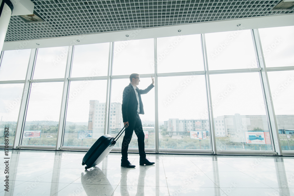 The businessman walk with a suitcase near panoramic windows in airport