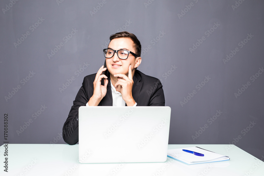 Happy young businessman talking on cell phone and using laptop in office Happy young businessman talking on cell phone and using laptop in office