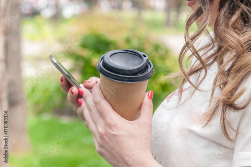 hands using a phone texting on smartphone app and holding paper cup of coffee