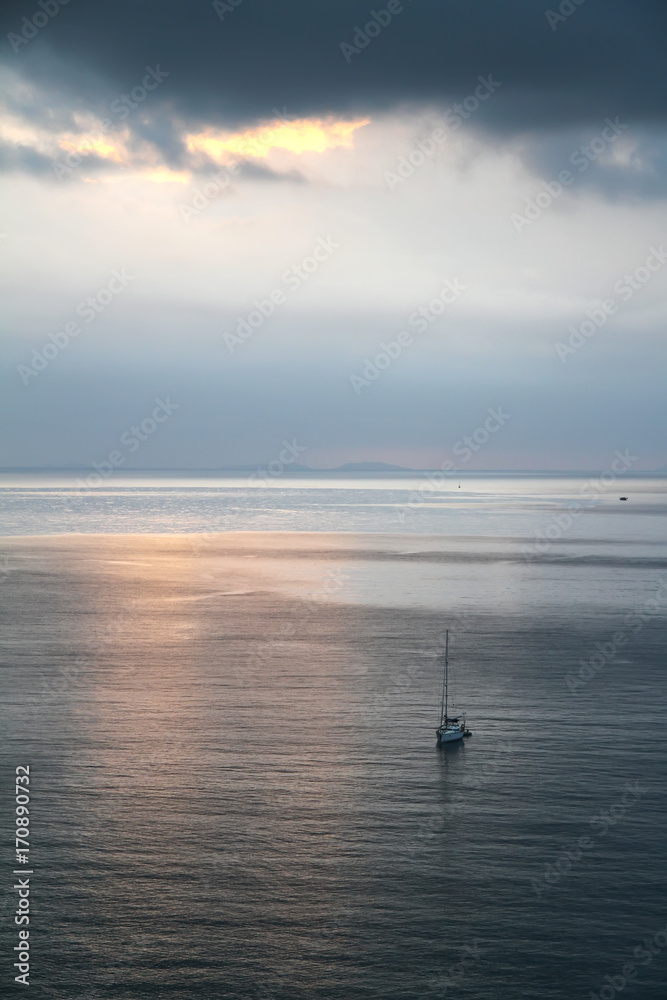 Calm evening sea with a yacht in front of a thunder-storm