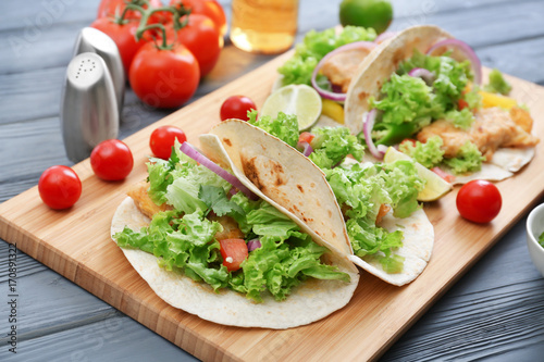 Wooden board with delicious tacos on kitchen table