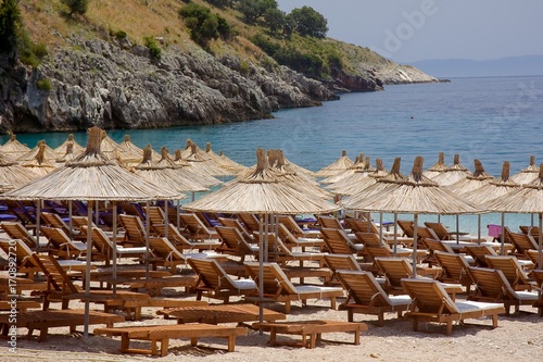 beach couches and straw parasols ready for customers on a summer day on the adriatic coast of Albania photo