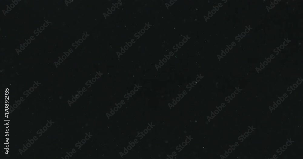 White particles and ink slowly moving in water on black background