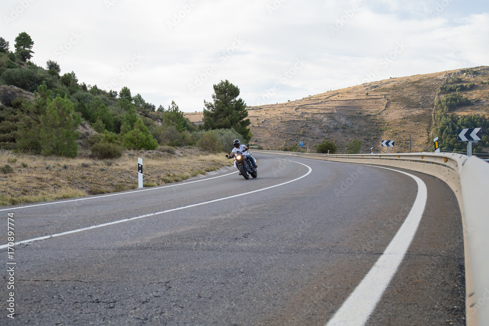 Fototapeta premium Young man riding a motorcycle on road turning in a curve in the mountains on sunny day. 