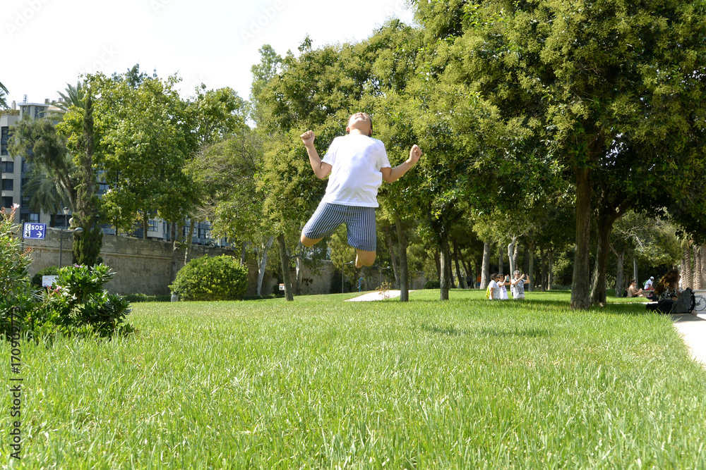 A boy is happy jumping on green juicy grass in a park