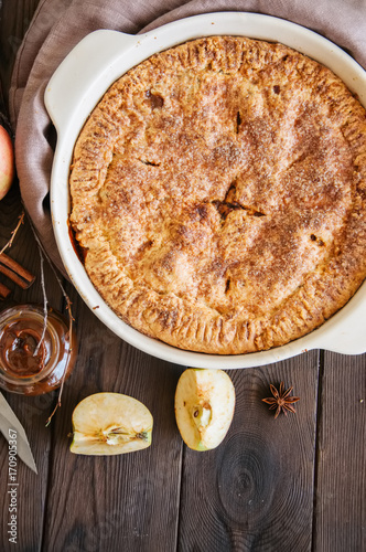 Traditional American apple pie in a ceramic form and ingredients on a wooden table. Close up and overhead view.