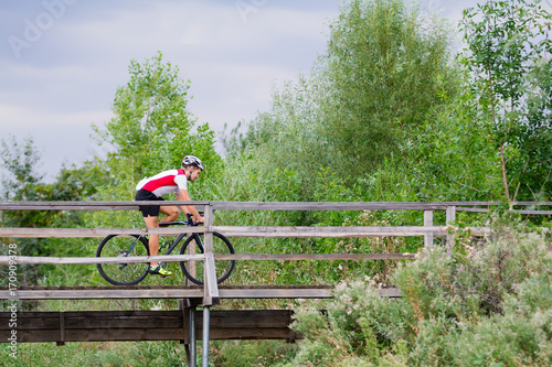 Professional bicucle rider in uniform and helmet on the old wooden bridge, country side background   photo