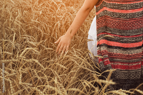 Young woman walking through field and touches wheat