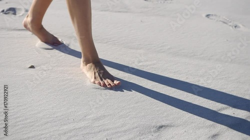 Barefooted woman walks on white sand in a sunny day photo