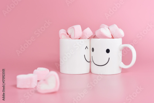 Two happy cups with marshmallows in the shape of heart on pink pastel background. Concept about love and relationship. Creative colorful greeting card. Lovely couple with happiness.