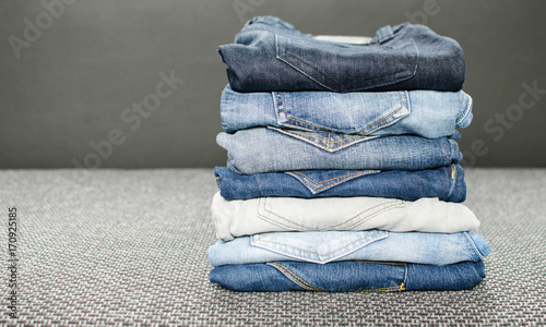 Pile of different jeans on gray background.