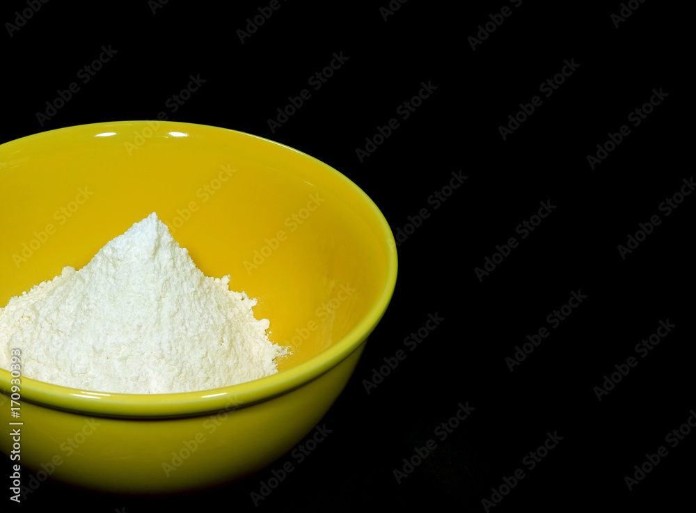 Pure white raw flour in yellow ceramic mixing bowl, isolated on black background with free space for design and text 