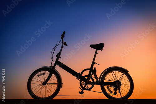 Silhouette bicycle on dramatic sky at sunset.