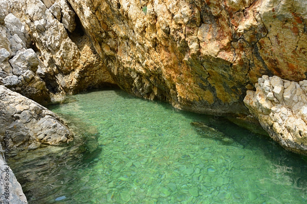 Small croatian shore cove hidden between steep cliffs with clear azure water and stony bottom