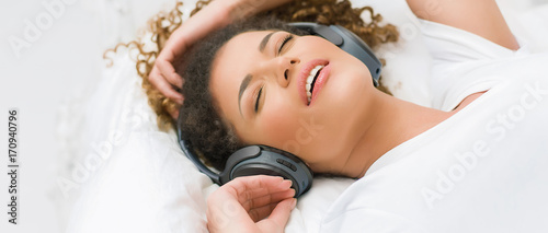 Beautiful woman portrait lying on bed and listening to relaxing music, letterbox