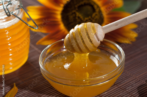 Natural honey in jar with dipper and sunflower on a wooden mat, close-up