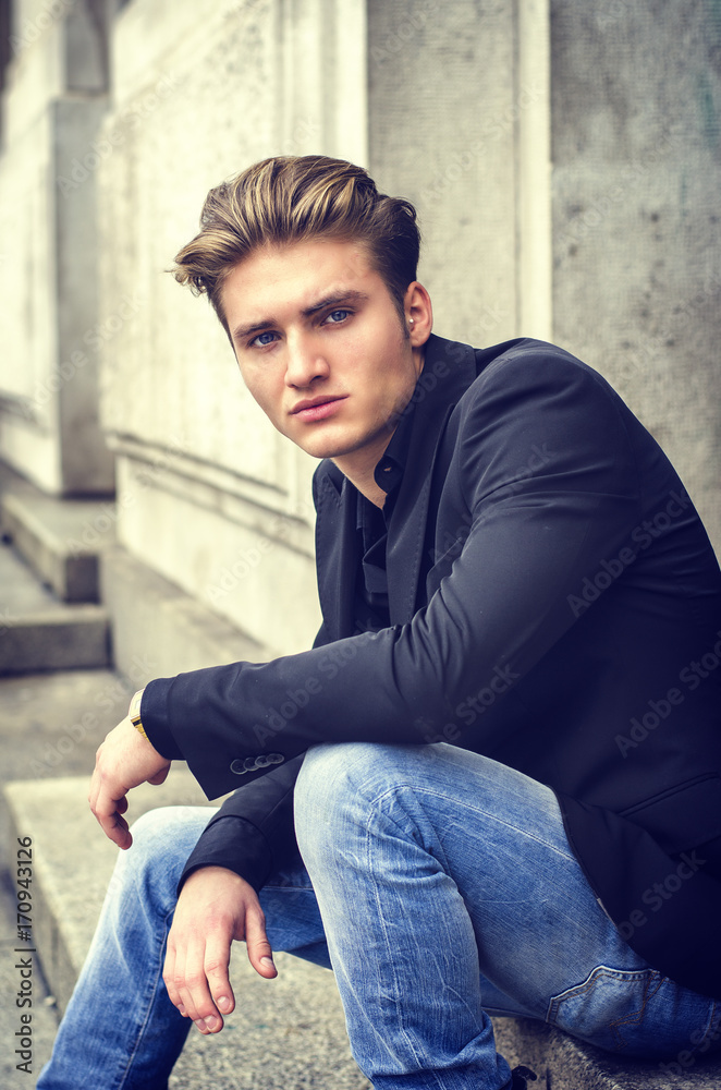 Handsome blond young man sitting on stone stair steps outside of big door Handsome blond young man sitting on stone stair steps outside of big door