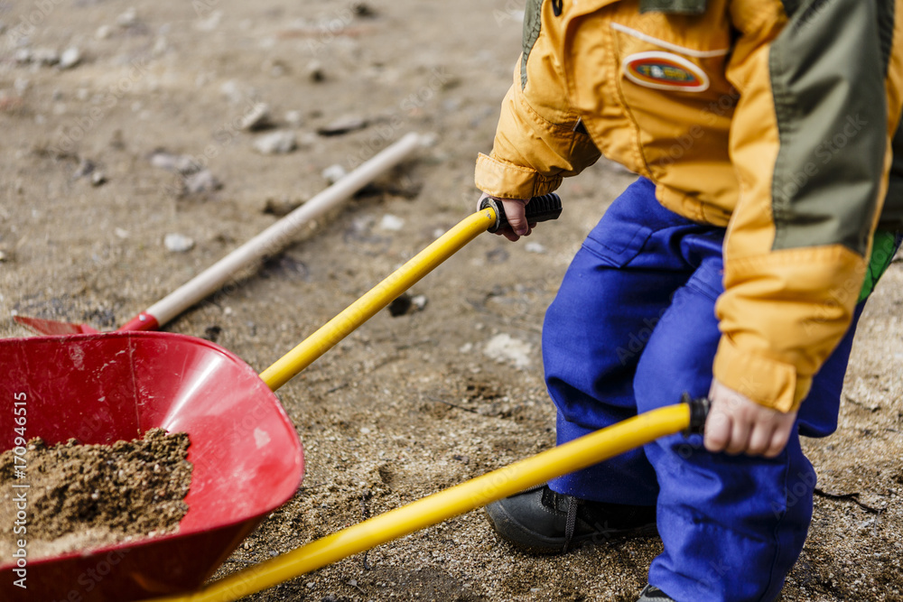 child play with sand, red shovel and small cute barrow child play with sand, red shovel and small cute barrow