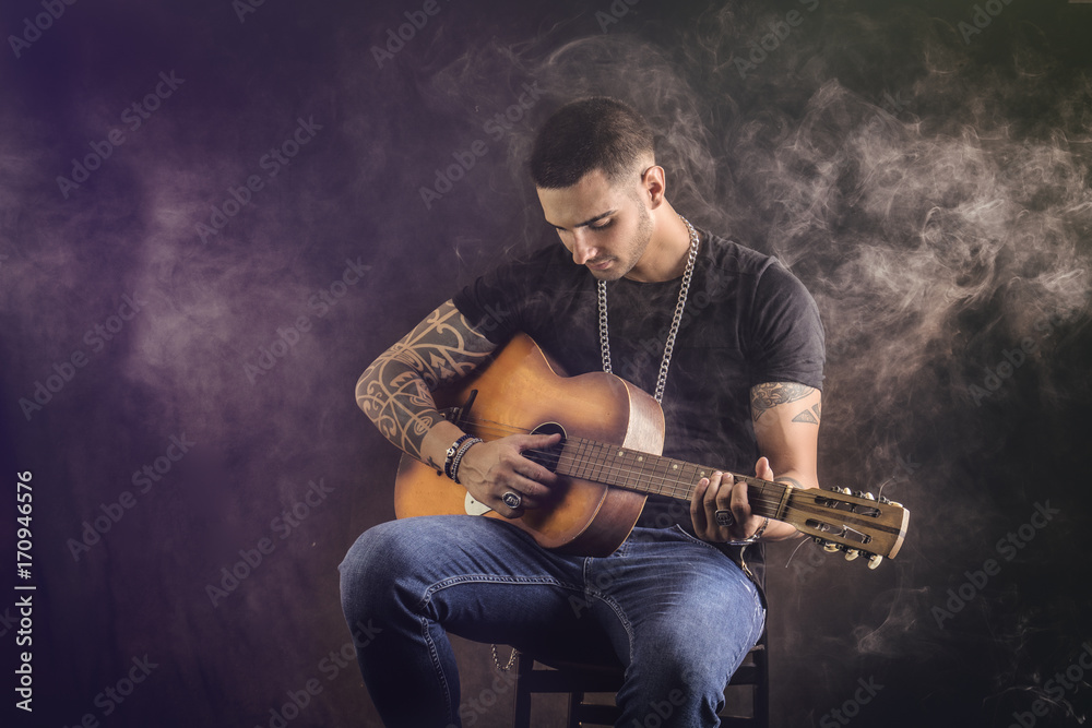 Obraz premium Portrait of hipster playing guitar against black background, in studio shot