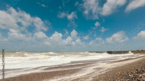 Crashing waves coming up on the shore of the English channel beach in Normandy, France. 4K time lapse. Stormy sea at the port of Dieppe on a bright summer day, clouds in the blue sky