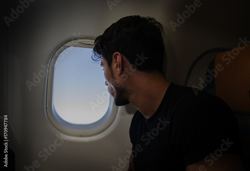 Tableau sur toile Side view of handsome young man against plane window sitting and looking out