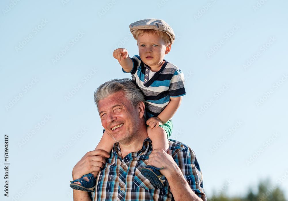 Grandfather carries grandson toddler boy on his shoulders