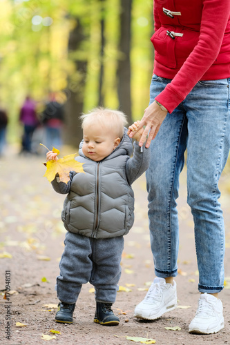 One year old baby boy in autumn park learning to walk with his mother.